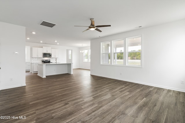unfurnished living room with visible vents, ceiling fan with notable chandelier, dark wood finished floors, recessed lighting, and baseboards