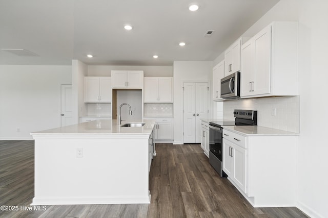 kitchen with a kitchen island with sink, a sink, white cabinetry, appliances with stainless steel finishes, and dark wood-style flooring