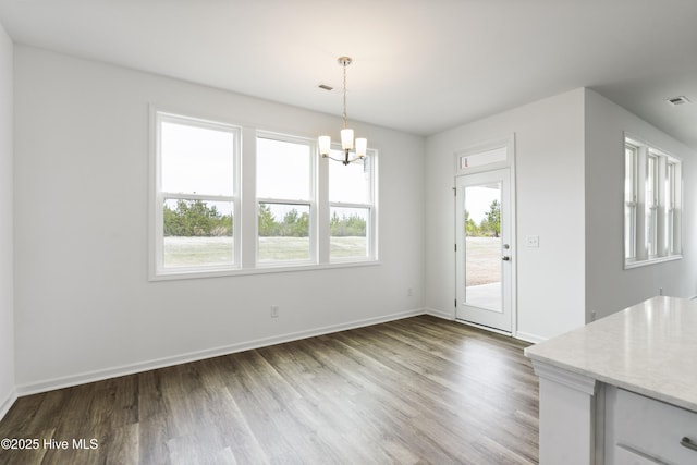 unfurnished dining area with an inviting chandelier, wood finished floors, baseboards, and visible vents