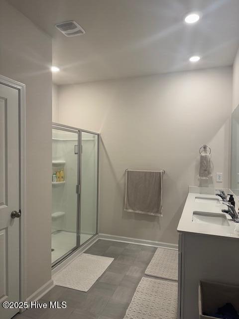 full bathroom with double vanity, a shower stall, visible vents, and baseboards