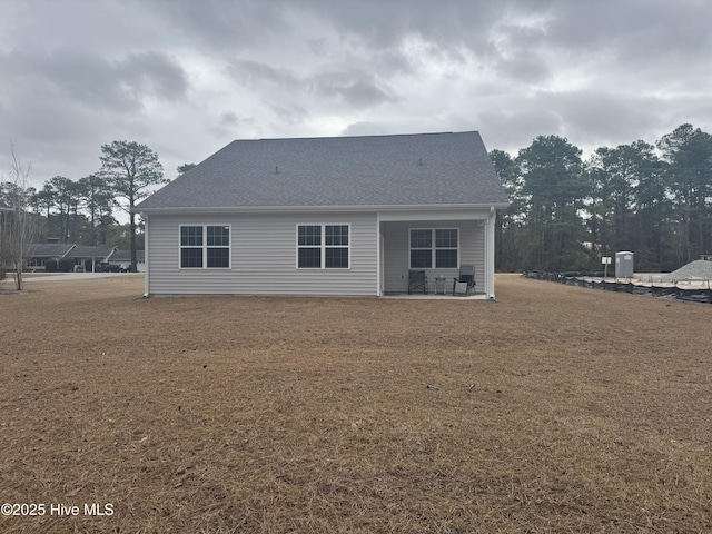 back of property featuring a shingled roof, a lawn, and a patio