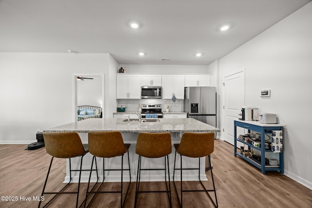 1507 Caracara Dr, New Bern, NC 28560 - kitchen with appliances with stainless steel finishes, a center island with sink, white cabinetry, wood finished floors, and a kitchen bar