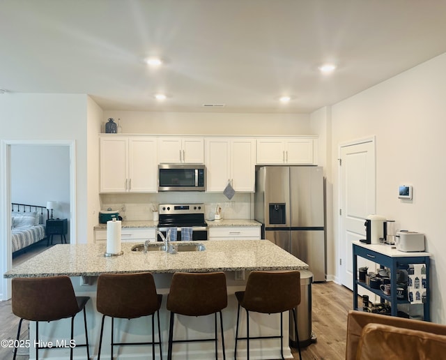 kitchen with white cabinets, a breakfast bar area, a kitchen island with sink, stainless steel appliances, and backsplash