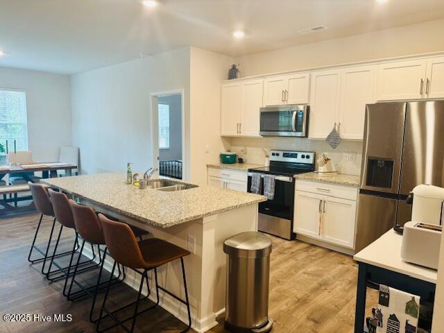 kitchen with light wood finished floors, appliances with stainless steel finishes, a breakfast bar, and a sink