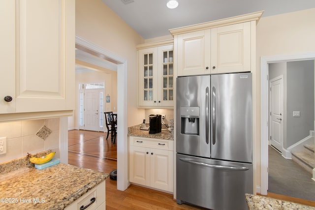 2906 Legends Dr, Southport, NC 28461 - kitchen featuring stainless steel refrigerator with ice dispenser, light wood finished floors, glass insert cabinets, light stone countertops, and decorative backsplash