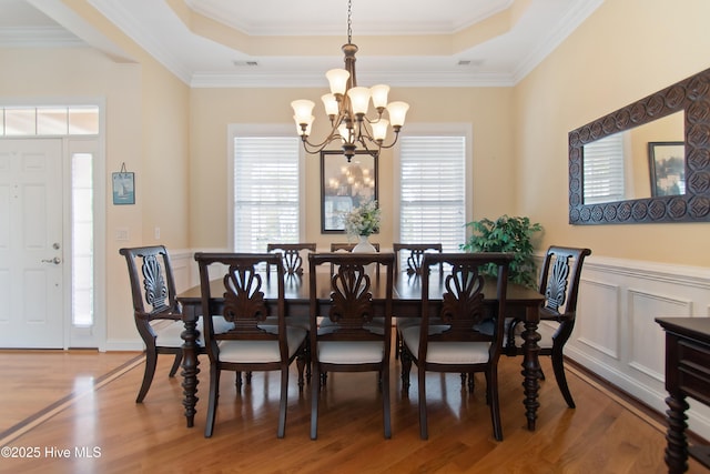 2906 Legends Dr, Southport, NC 28461 - dining room with a chandelier, a raised ceiling, light wood-style floors, healthy amount of natural light, and a wainscoted wall