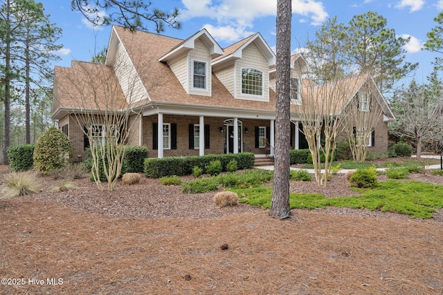 cape cod home with covered porch, brick siding, and roof with shingles