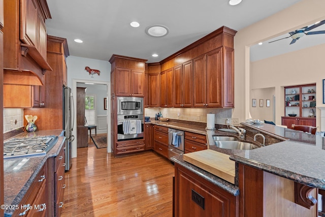kitchen with dark stone countertops, a peninsula, light wood finished floors, and stainless steel appliances