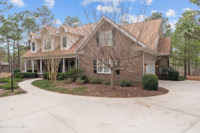 cape cod-style house featuring covered porch, concrete driveway, brick siding, and a shingled roof