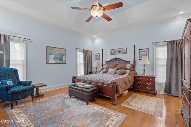 bedroom featuring baseboards, light wood-style floors, a tray ceiling, and ornamental molding