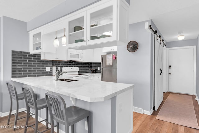 kitchen with light wood finished floors, a barn door, a peninsula, white cabinets, and white appliances