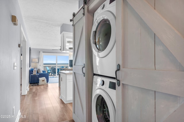 washroom featuring a textured ceiling, a barn door, light wood finished floors, stacked washer / drying machine, and laundry area