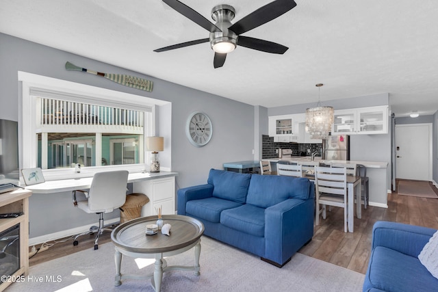 living room with baseboards, wood finished floors, built in desk, and ceiling fan with notable chandelier