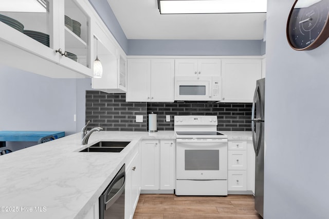 kitchen with light stone countertops, light wood-style flooring, white cabinets, white appliances, and a sink