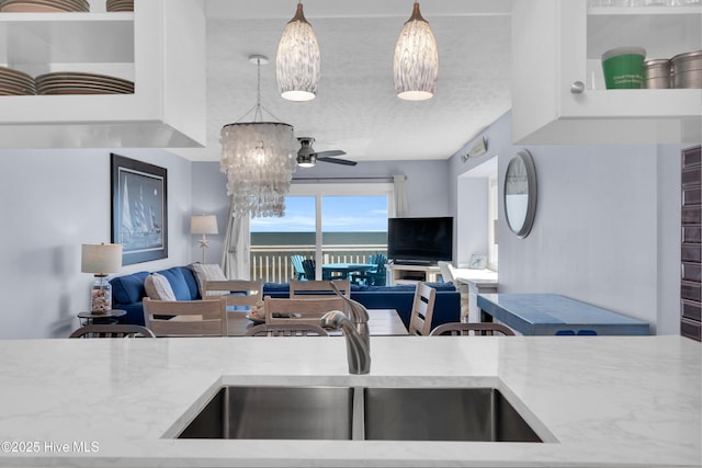 kitchen featuring a sink, hanging light fixtures, a textured ceiling, ceiling fan with notable chandelier, and open floor plan