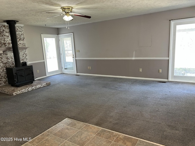 unfurnished living room with a wealth of natural light, carpet flooring, and a wood stove