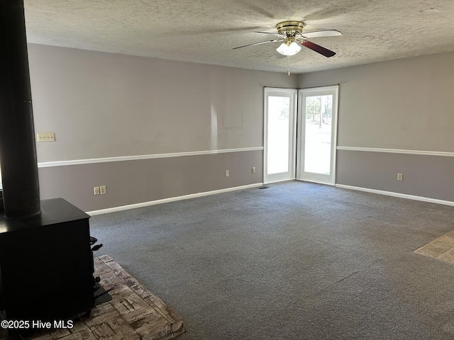 unfurnished room featuring baseboards, carpet floors, a wood stove, ceiling fan, and a textured ceiling