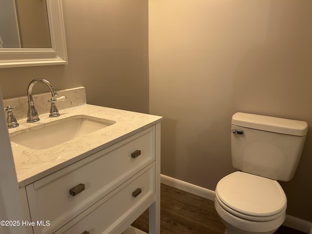 half bath with toilet, vanity, baseboards, and wood finished floors