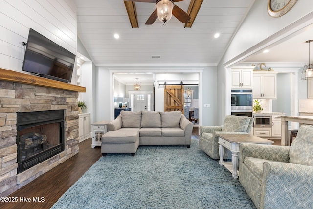 living room with a ceiling fan, vaulted ceiling with beams, dark wood-style flooring, a stone fireplace, and a barn door