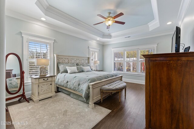 bedroom with multiple windows, a raised ceiling, wood finished floors, and crown molding