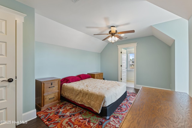 bedroom featuring a ceiling fan, baseboards, dark wood-style flooring, vaulted ceiling, and connected bathroom