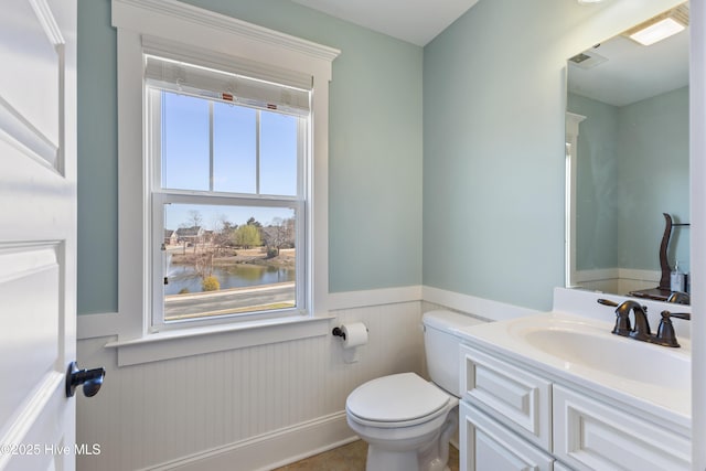 bathroom featuring vanity, toilet, visible vents, and wainscoting