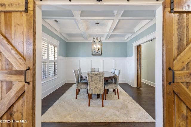 dining space featuring coffered ceiling, dark wood finished floors, an inviting chandelier, beam ceiling, and a barn door