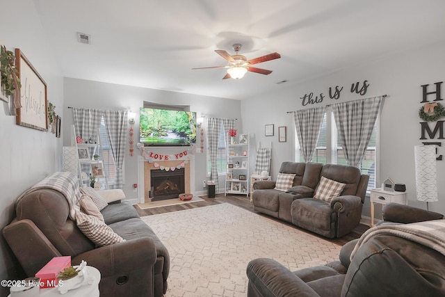 living area with visible vents, a ceiling fan, wood finished floors, and a tiled fireplace