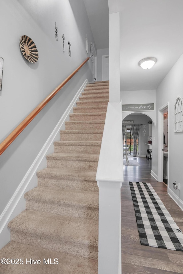 stairway featuring wood finished floors, arched walkways, and baseboards