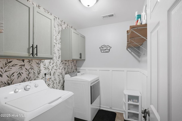 clothes washing area featuring visible vents, wainscoting, washer and dryer, a decorative wall, and cabinet space