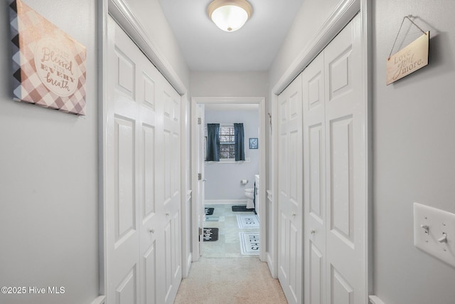 hall with baseboards and light colored carpet