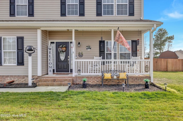 doorway to property featuring fence, a lawn, and covered porch