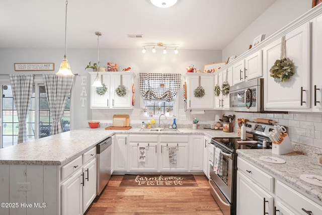 kitchen with a peninsula, a sink, appliances with stainless steel finishes, white cabinetry, and light wood-type flooring