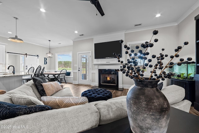 living area featuring a warm lit fireplace, a barn door, recessed lighting, wood finished floors, and crown molding