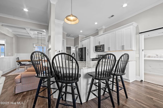 kitchen featuring dark wood finished floors, stainless steel microwave, white cabinetry, wainscoting, and light stone countertops