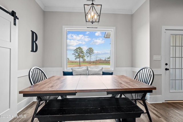 dining space featuring ornamental molding, a barn door, wainscoting, and wood finished floors