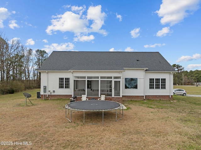 rear view of property featuring a sunroom, crawl space, a lawn, roof with shingles, and a trampoline