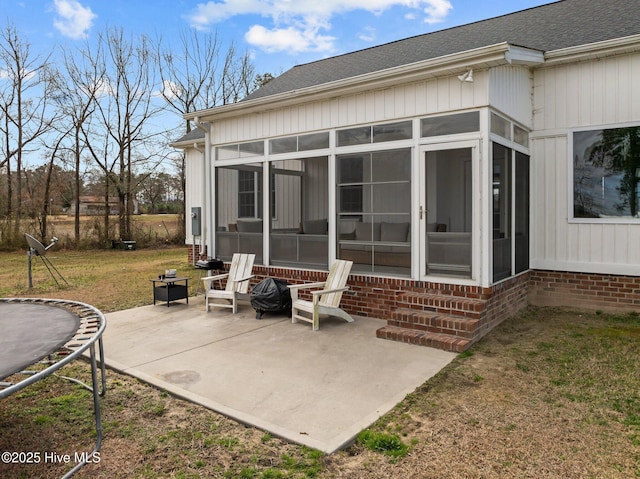 back of property featuring a trampoline, roof with shingles, a yard, a sunroom, and a patio area