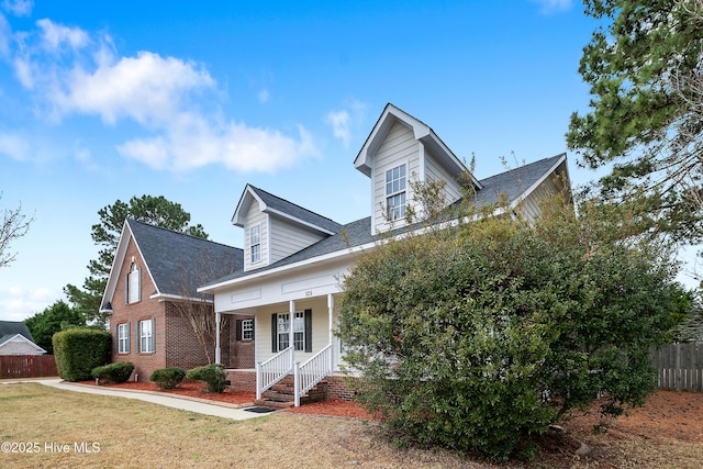 new england style home with brick siding, a front yard, fence, and covered porch