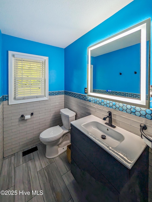 13596 Hobbton Hwy, Newton Grove, NC 28366 - half bathroom featuring tile walls, toilet, wainscoting, vanity, and a textured ceiling