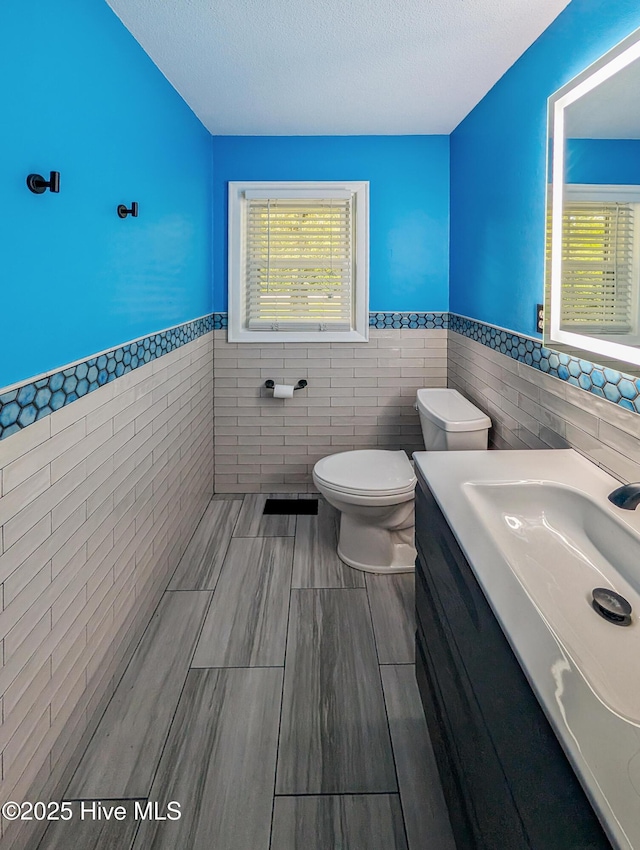 13596 Hobbton Hwy, Newton Grove, NC 28366 - bathroom with tile walls, a wainscoted wall, toilet, vanity, and a textured ceiling