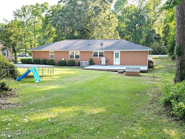 13596 Hobbton Hwy, Newton Grove, NC 28366 - back of property featuring a wooden deck, a lawn, a trampoline, brick siding, and central air condition unit
