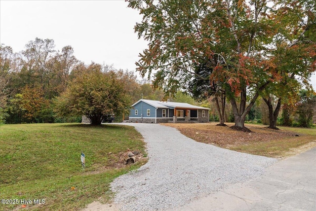 single story home with gravel driveway, stone siding, and a front yard