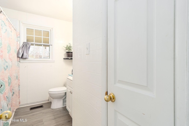 full bath featuring a shower with shower curtain, toilet, wood finished floors, and visible vents