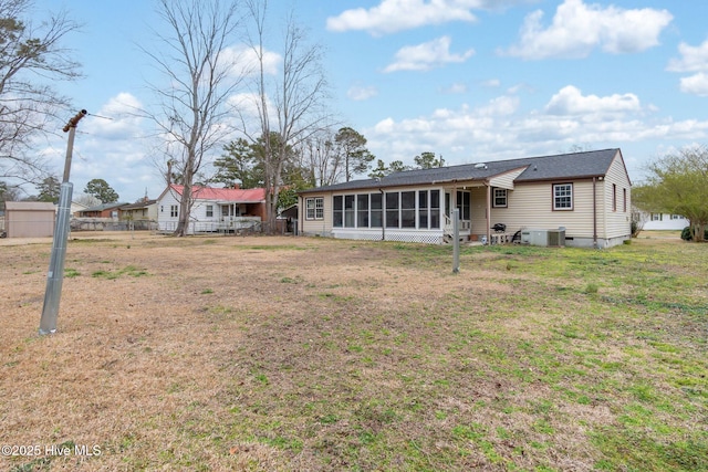 rear view of property with central air condition unit, a lawn, fence, and a sunroom