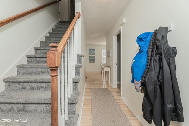 stairway featuring a textured ceiling, wood finished floors, and baseboards