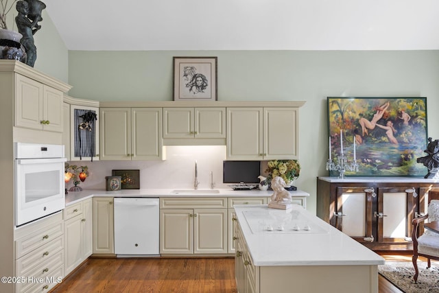 kitchen featuring dark wood finished floors, light countertops, cream cabinetry, white appliances, and a sink