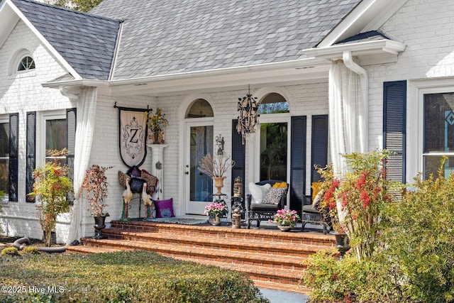 entrance to property featuring covered porch, brick siding, and a shingled roof