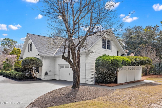 view of home's exterior featuring brick siding, fence, concrete driveway, roof with shingles, and an attached garage