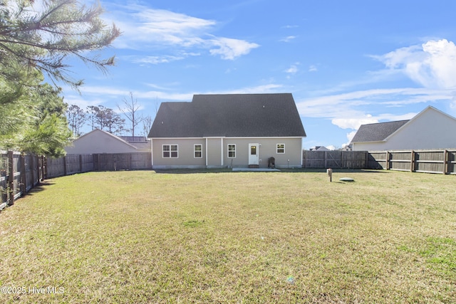 back of house with a fenced backyard, roof with shingles, and a lawn